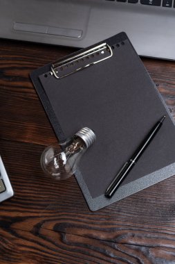 Kalemle siyah bir defterin üzerinde duran ampul. Elektrik, enerji, fikirler ve yaratıcı düşünce anlayışı minimalist bir çalışma alanında. Dikey kart.