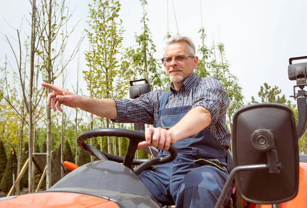 gardener in overalls behind the wheel of a tractor, shows his hand away