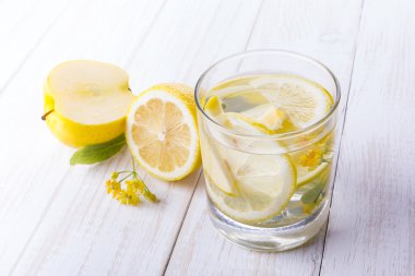 Bir bardak limon elma meyve ahşap beyaz masa su ile. Limon ve ıhlamur çiçek.