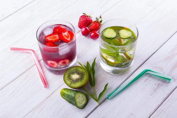 Two cups of fruit with water and tubules near kiwi, cucumber, mint, strawberry, cherry — Stock Photo, Image