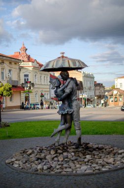 Şehir parkında bir çiftin bronz heykeli şemsiye altında öpüşüyor. Romantizmi, aşkı, randevuyu temsil eder.