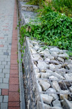 Gabion duvarı bir yolu yeşillikten ayırır. Modern, sürdürülebilir manzara tasarımı. Erozyon için kullan