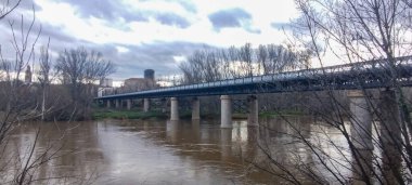 İspanya 'nın Logroo şehrinde kışın karanlık sularla kaplı uzun metal çerçeveli bir köprü.