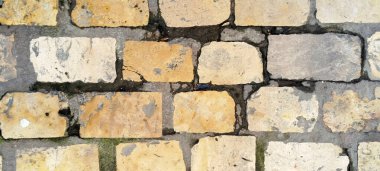 Yıpranmış dokuları ve gri çimento eklemleri olan eski bir taş kaldırımın üst görüntüsü