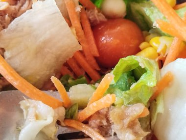 Taze salatadaki çatalın yakın çekimi, marul, havuç, ton balığı, mısır ve vişneli domates.