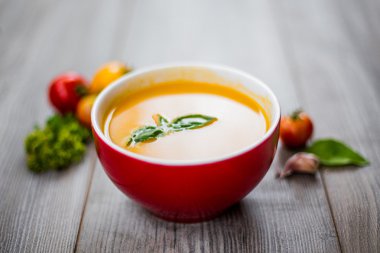 Ahşap bir arka planda sebzeli domates çorbası ve otlar.