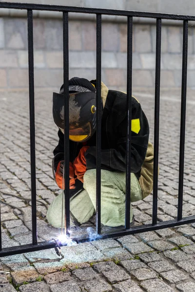 Kaynakçı Kaynak çit parmaklıklar üzerinde. Koruyucu elbise ve siyah bir maske takmak.