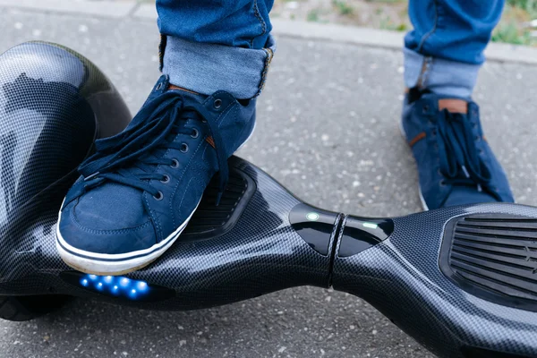 Leg men in blue sneakers and jeans standing on the blue gyroscooter platform, which is on the street. Start to using the electrical scooter, hoverboard, gyroboard or gyroscooter.