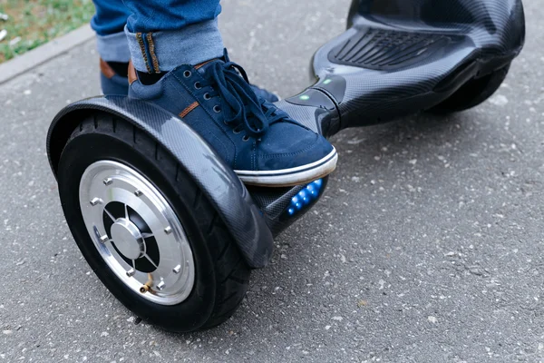 Been mannen in blauwe sneakers en jeans staande op het platform van de blauwe gyroscooter, die op de straat. Start met behulp van de elektrische scooter, hoverboard, gyroboard of gyroscooter. — Stockfoto