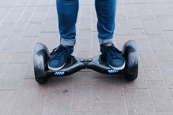 De man in blauwe jeans en sneakers rijdt een blauwe elektrische scooter, hoverboard, gyroboard of gyroscooter. Twee voeten staan op een platform. — Stockfoto