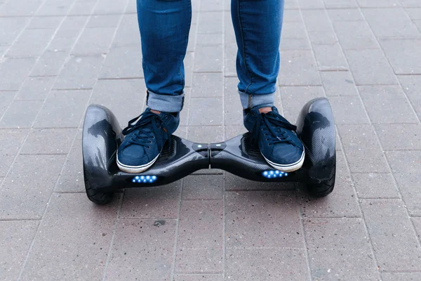 Adam mavi kot pantolon ve spor ayakkabı ile mavi elektrikli scooter, hoverboard, gyroboard veya gyroscooter gidiyor. Ayakları bir platformda ayakta.