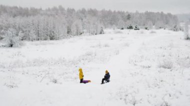 Çocuklar karlı bir ormanın arka planında oynuyorlar. Kışın ölüsü, soğuk hava, buz, kar