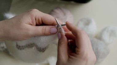  Kadınların elleri yakın plan: Yelken şampanyası renginde gri ve pudralı yün örülmüş bir ürün. 