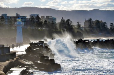 Big waves breaking over Wollongong harbor breakwall and lighthouse clipart