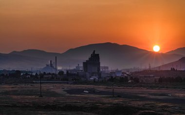 Güneş doğarken sisli bir günde parlak turuncu gökyüzü ile kömür santrali elektrik santralini yaktı.