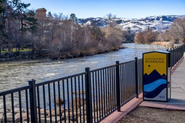 Reno şehir merkezindeki Wingfield Parkı 'ndaki Truckee Nehri' nde karlı dağlar ve arka planda açık mavi bir gökyüzü var..