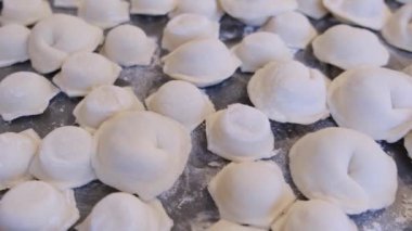 Pişmemiş hamur tatlısı, Pelmeni un dolu bir masada yatıyor.