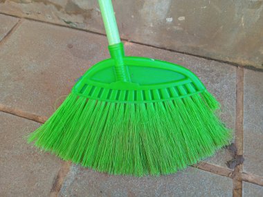 Döşeme üzerinde plastik tüyleri olan yeşil bir süpürge..