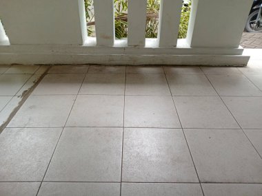 Temiz ve bakımlı fayansları, arka planda parmaklıkları ve dışarıdaki yeşillikleri gösteren görünür dikişli fayanslı bir döşeme.