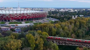 Warsaw, Poland - October 5, 2025: Passenger trains pass over the bridge in front of the National Stadium in Warsaw