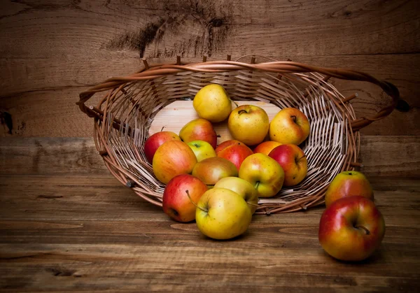 Äpfel sitzen in einem Holzkorb auf hölzernem Hintergrund — Stockfoto