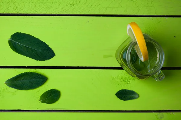 Limonada con lima, menta en un frasco sobre una mesa de madera verde — Foto de Stock
