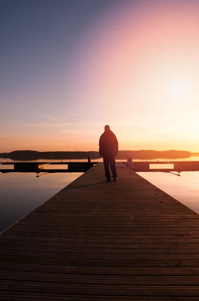 Bir adam ahşap iskele üzerinde günbatımında gider.
