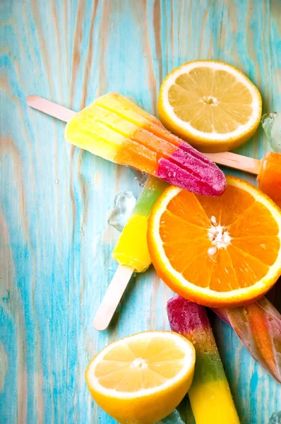 Colorful ice lolly and friuts on blue wooden background