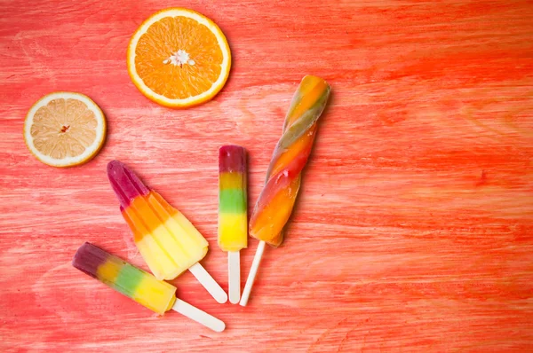 Kleurrijke ice lolly op een rode houten achtergrond — Stockfoto