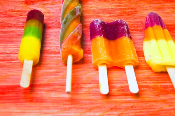 Colorful ice lolly on a red wooden background — Stock Photo, Image