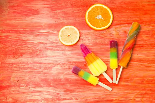 Kleurrijke ice lolly op een rode houten achtergrond — Stockfoto