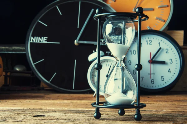 Hourglass and ticking clocks on old wooden table