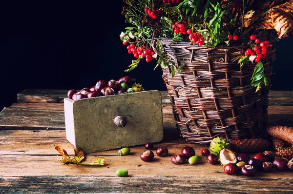 Verdorde bladeren, herfst bloemen en kastanjes in een rieten mand — Stockfoto