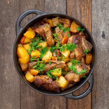 Tahta masa yüzeyinde patates ve kuzu eti olan güveç.