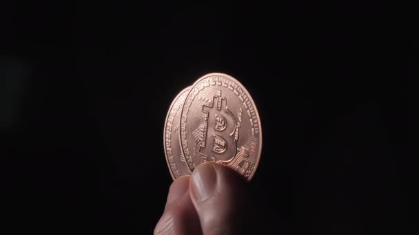 Bitcoin-Münzen zwischen den Fingern. Schwarzer Hintergrund, leerer Raum — Stockvideo