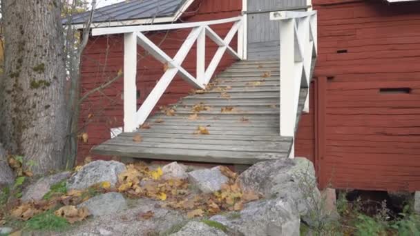 Die verstreuten Ahornblätter auf dem Boden mit dem roten Gebäude in Finnland — Stockvideo