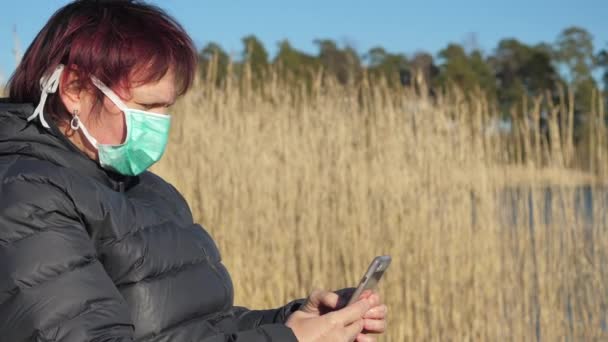 Жінка в її масці для обличчя тримає телефон під час карантину — стокове відео