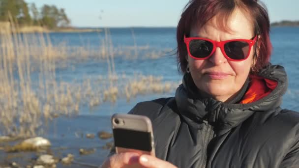 赤いサングラスをかけた女性がフィンランドの携帯電話で自撮り — ストック動画