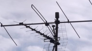 Arka planda bulutlu gökyüzü olan bir çatıdaki antenlerin yakın plan görüntüsü.