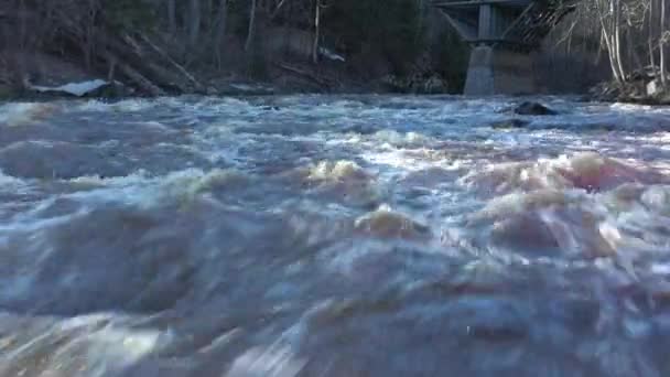 Closeup aerial shot of a rapid river flowing under a bridge. — Vídeo de stock