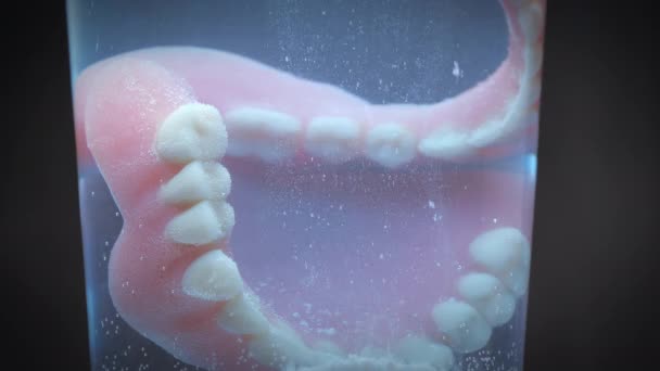 Closeup shot showing dentures being cleaned by a glass full of cleaning fluid. — Stock Video