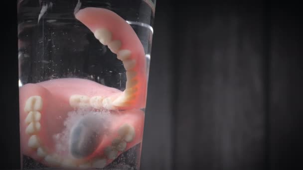 Primer plano de una tableta limpiadora de dientes de prótesis cayó en un vaso de agua. — Vídeo de stock