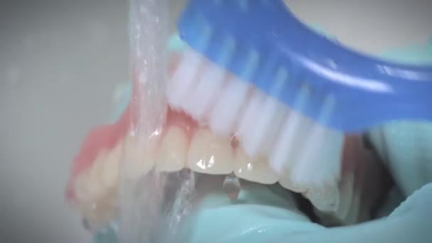 Close-up schot tonen poetsen van prothese tanden met stromend water. — Stockvideo
