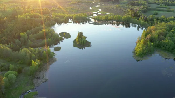 Hava perspektifi, canlı yeşil ağaçlar ve dolambaçlı bir nehirle çevrili, doğanın güzelliğini ve barışçıl manzarayı yansıtan küçük adalarla dolu sakin bir göl sergiliyor. Ao, Estonya.