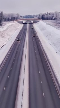 Estonya 'daki soğuk İskandinav kışında yüksek açılı bir otoyol manzarası. Hava bulutlu. Karlı orman ve toprak. Araba sürüyor. İnsansız hava aracı yavaşça ilerliyor.