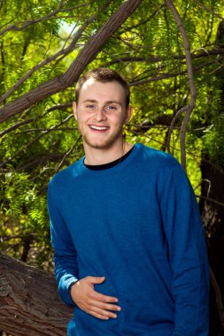 Ağaca yaslanmış gülümseyen genç adam