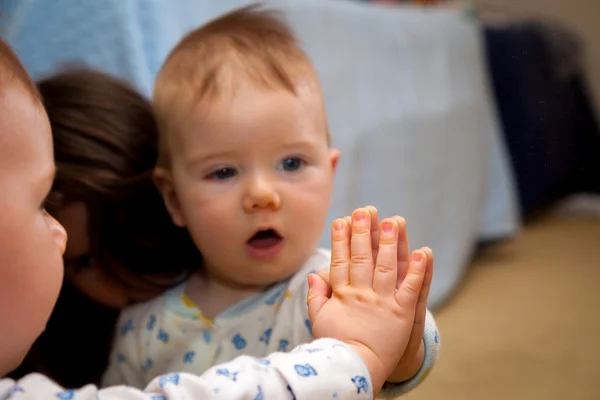 Bebê segura a mão em um espelho e é surpreendido pela reflexão — Fotografia de Stock