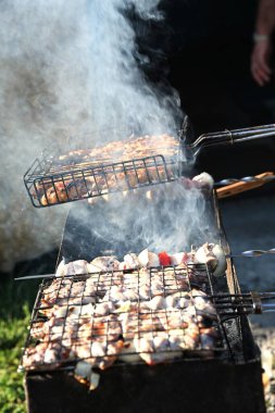 Izgara rafındaki et parçalarını ve şişleri gösteren yüksek çözünürlüklü dikey görüntü. Yükselen duman, ticari kullanım için sıcak ve lezzetli yemek pişirme sürecini vurguluyor.