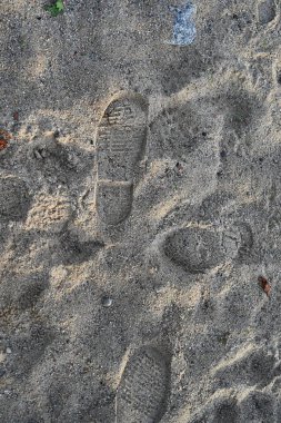 Yukardan aşağı nemli manzara, kabataslak kum, ayakkabı ve ayak izleri. Sıcak, dünyevi tonlar ve küçük enkaz parçaları seyahat ve tatil temaları için ideal zengin bir doğal doku arka planı oluşturur..