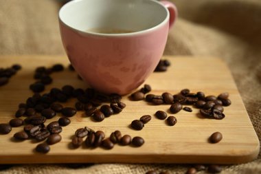 Kahveyle dolu pembe seramik bardağın üstü düz yatıyordu. Tahta bir tahta üzerinde kavrulmuş kahve çekirdekleri ve çuval bezi ile çevriliydi. Kafe temaları için sıcak, rahat bir sabah havası yaratır.